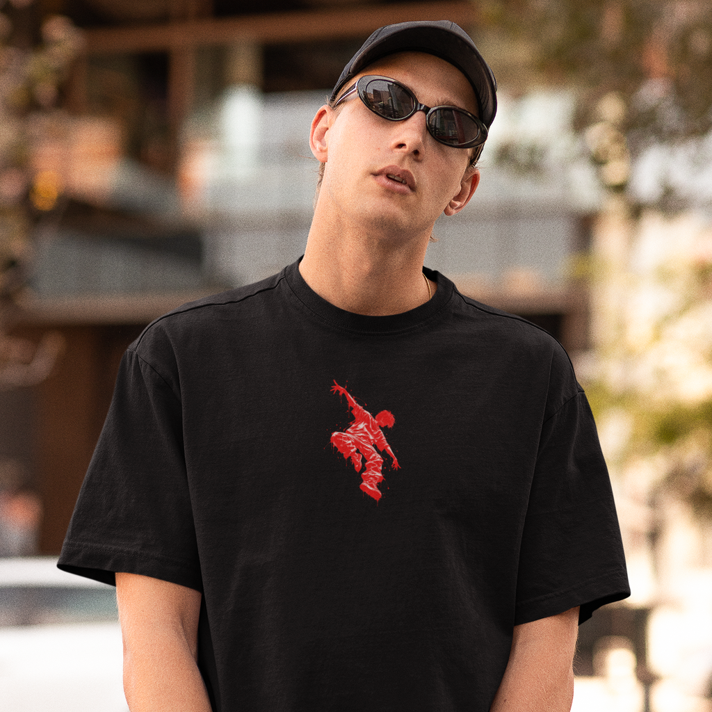A man wearing a black crewneck t-shirt with a red graphic of a person jumping over a basketball on the chest, paired with a black cap and sunglasses, standing outdoors on a blurred street background.