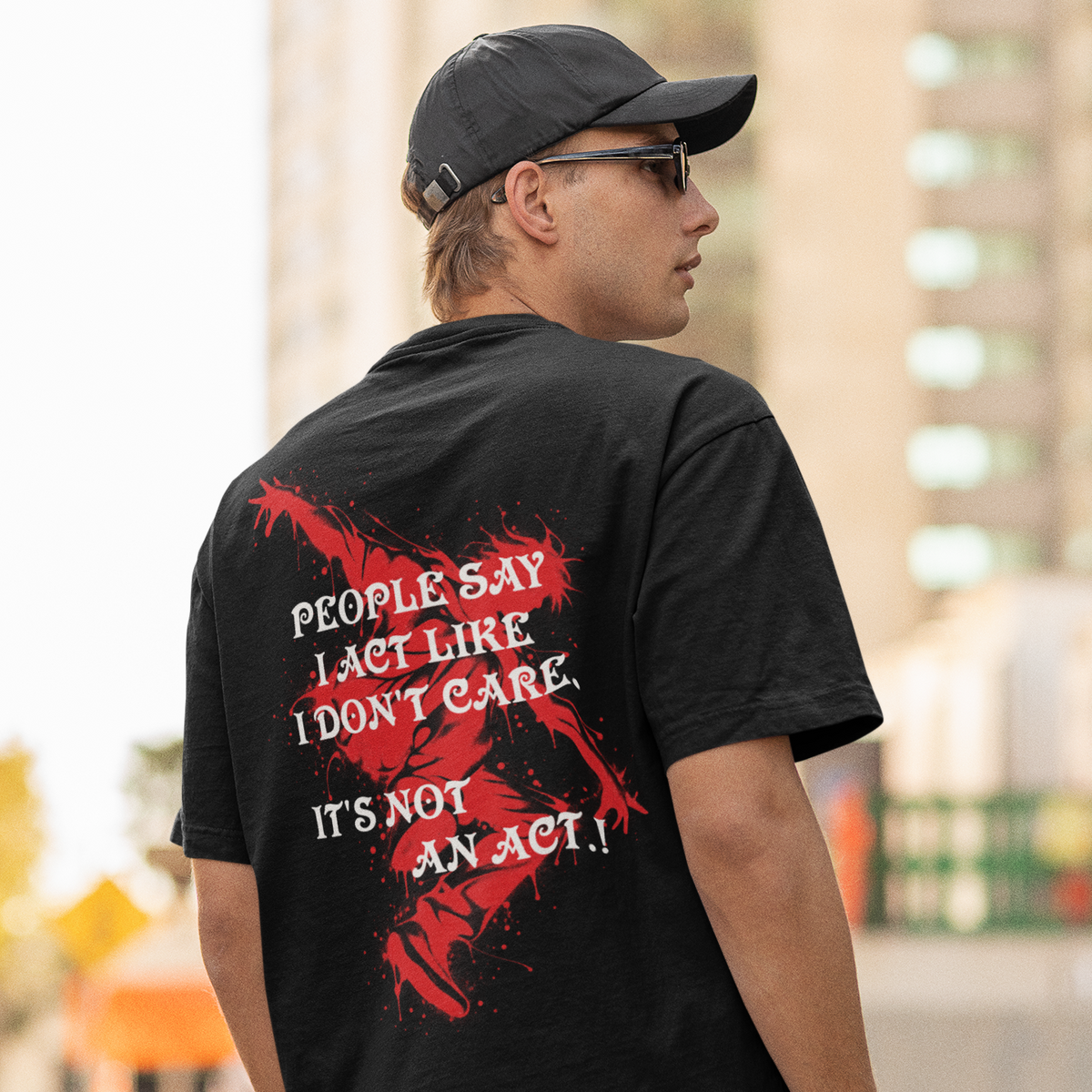 A man wearing a black t-shirt with a red and white graphic text print on the back, photographed from behind in an outdoor urban setting.