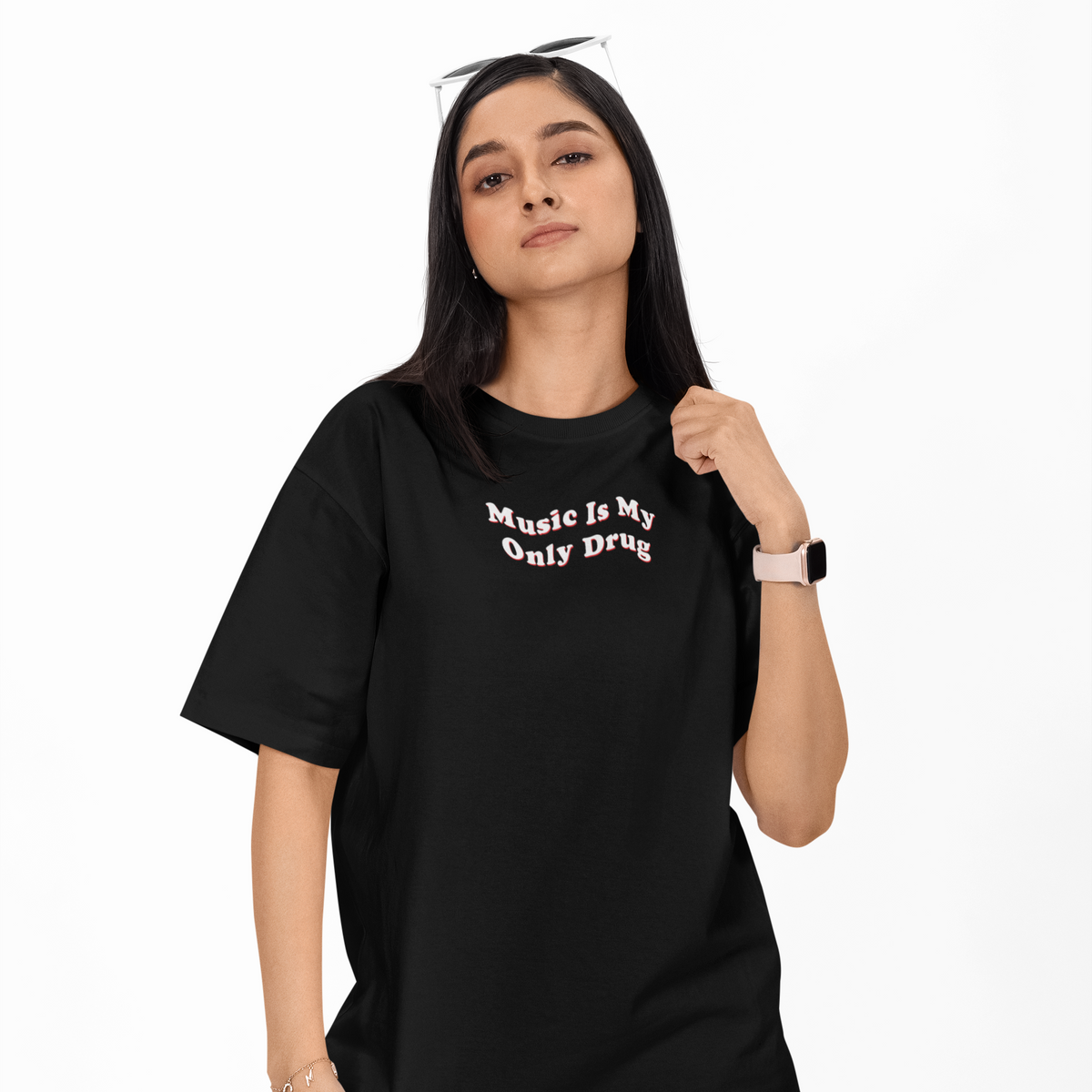 A woman modeling a black oversized t-shirt with the text 'Music is My Only Drug' printed in white on the chest, paired with gray cargo pants against a plain white background.